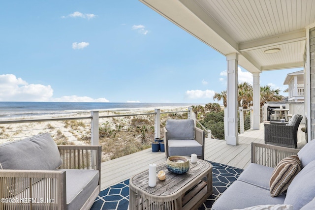 deck featuring an outdoor living space, a water view, and a beach view