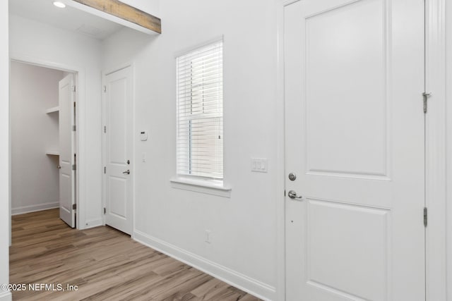 foyer featuring beam ceiling, baseboards, and light wood finished floors