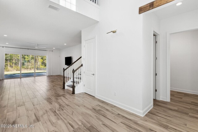 unfurnished living room with light wood-type flooring, stairway, baseboards, and visible vents