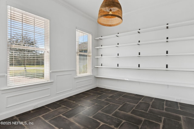 unfurnished dining area with brick floor, wainscoting, and crown molding