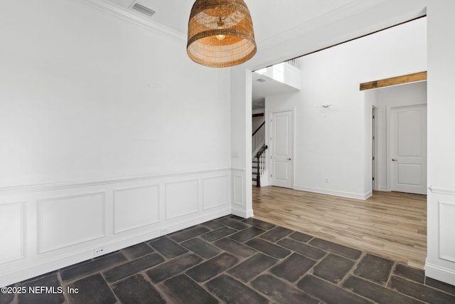 empty room featuring a wainscoted wall, visible vents, stairway, dark wood finished floors, and crown molding