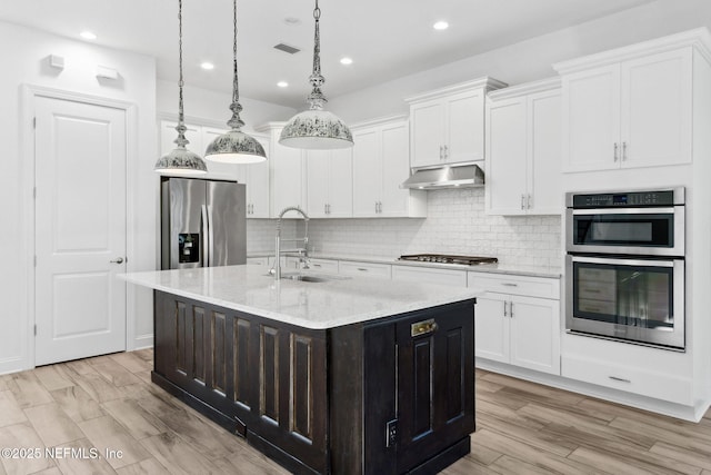 kitchen with stainless steel appliances, a sink, white cabinets, and under cabinet range hood