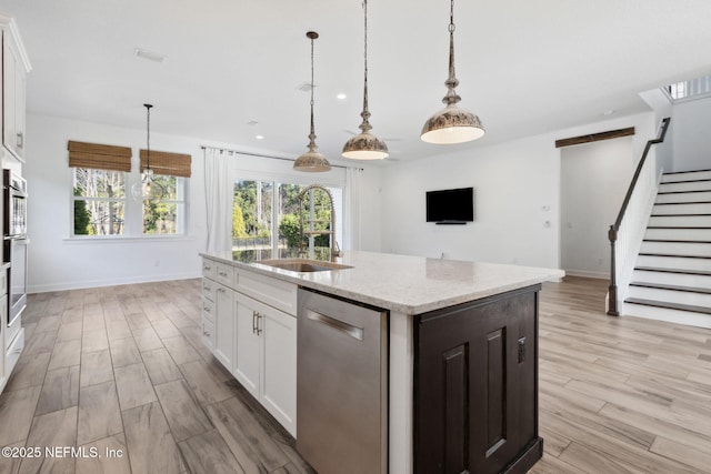 kitchen featuring a center island with sink, white cabinets, hanging light fixtures, light wood-style floors, and stainless steel dishwasher