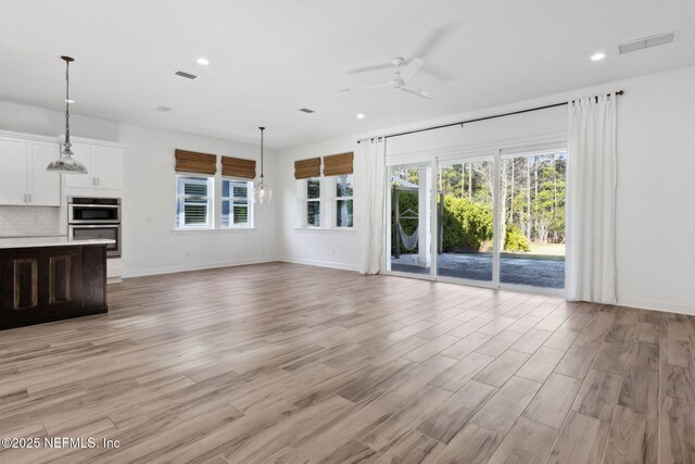 unfurnished living room with light wood-style flooring, a ceiling fan, visible vents, and a healthy amount of sunlight