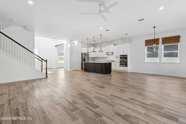 unfurnished living room featuring recessed lighting, stairway, ceiling fan, light wood-type flooring, and baseboards