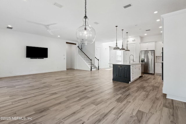 kitchen with white cabinetry, open floor plan, light countertops, stainless steel fridge with ice dispenser, and an island with sink