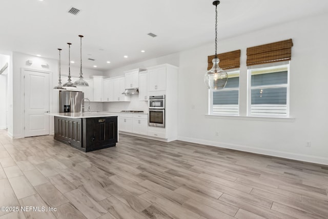 kitchen with stainless steel appliances, visible vents, light countertops, backsplash, and under cabinet range hood