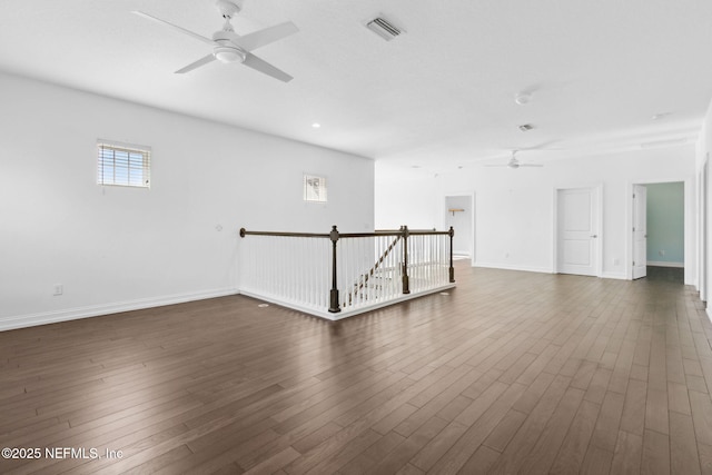 empty room with a ceiling fan, dark wood-style flooring, visible vents, and baseboards