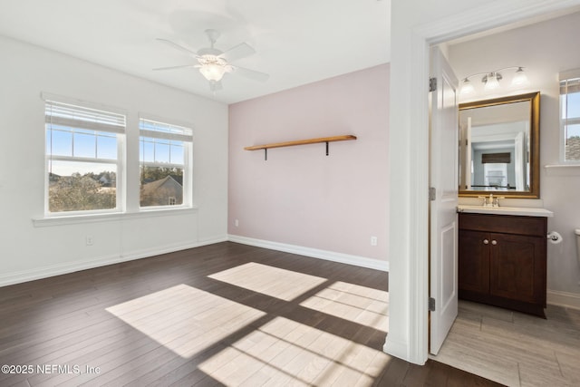 unfurnished bedroom featuring ceiling fan, a sink, baseboards, and wood finished floors