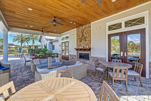 view of patio / terrace featuring an outdoor living space with a fireplace, ceiling fan, outdoor dining area, and french doors