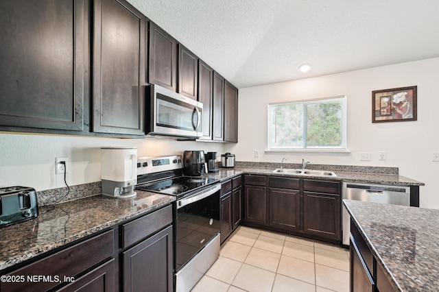 kitchen with appliances with stainless steel finishes, dark stone countertops, a sink, and dark brown cabinetry