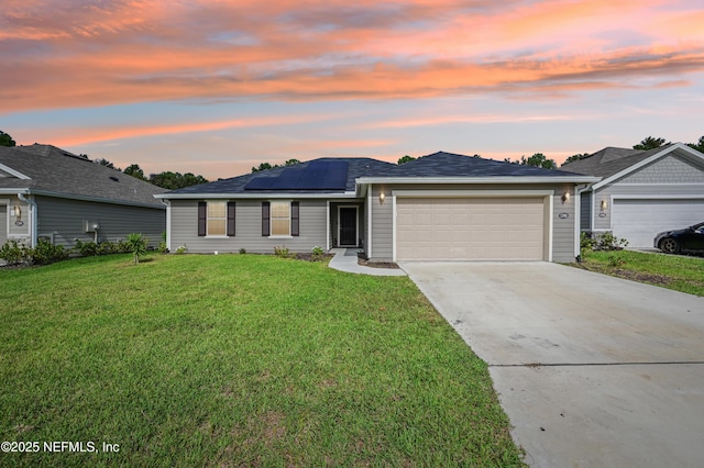 ranch-style house featuring a garage, driveway, solar panels, and a yard