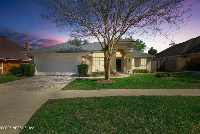 view of front of house with fence, stucco siding, a lawn, a garage, and driveway