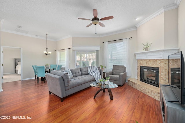 living room with ceiling fan with notable chandelier, crown molding, wood finished floors, and a fireplace