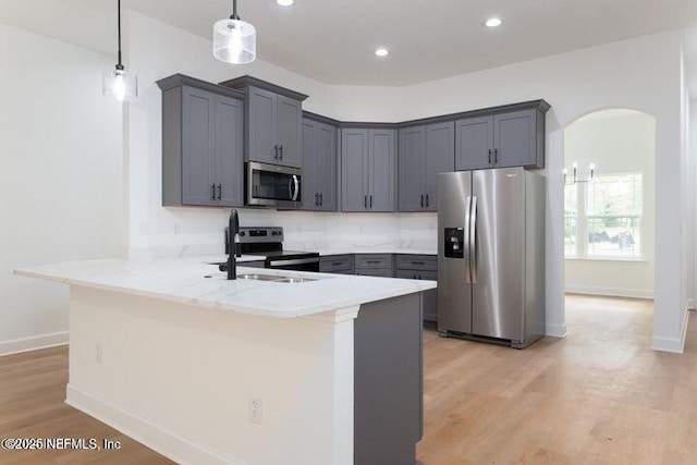 kitchen featuring appliances with stainless steel finishes, sink, hanging light fixtures, kitchen peninsula, and light wood-type flooring