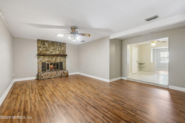 unfurnished living room featuring a stone fireplace, wood-type flooring, a textured ceiling, and ceiling fan