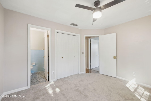 unfurnished bedroom with ensuite bathroom, light colored carpet, tile walls, a closet, and ceiling fan