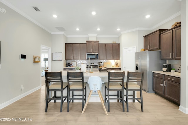 kitchen with a breakfast bar, stainless steel appliances, tasteful backsplash, light hardwood / wood-style floors, and an island with sink