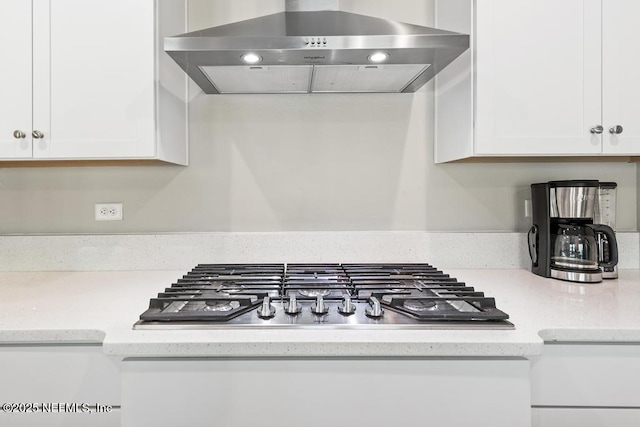 kitchen with stainless steel gas stovetop, light stone countertops, white cabinets, and wall chimney exhaust hood