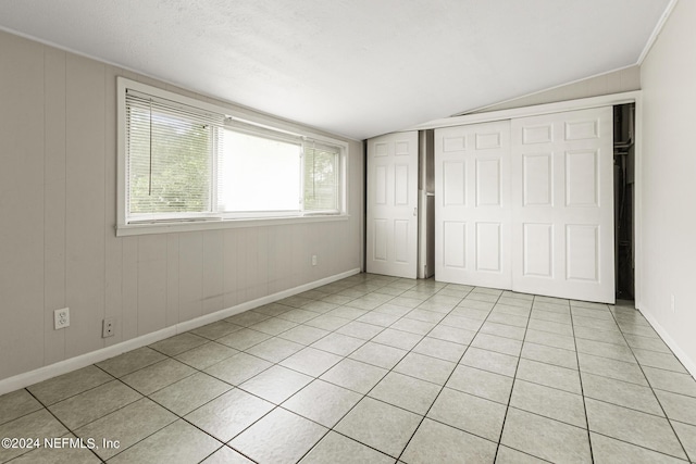 unfurnished bedroom with light tile patterned floors, vaulted ceiling, a closet, and wooden walls