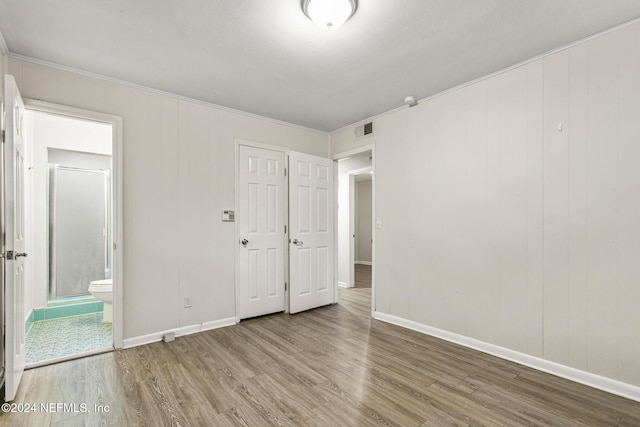 unfurnished bedroom with crown molding, ensuite bathroom, and hardwood / wood-style floors