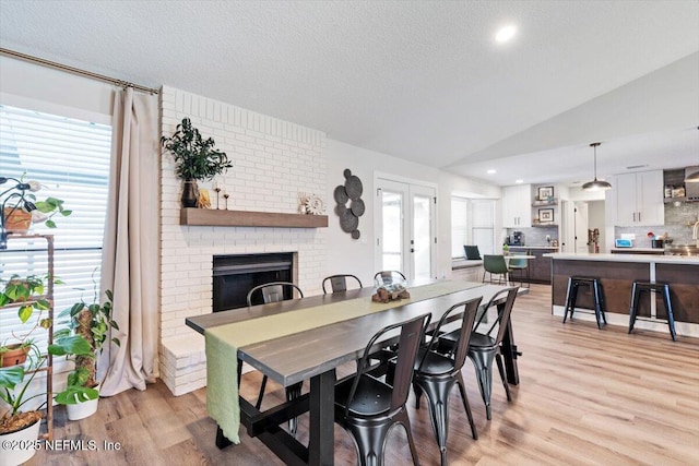 dining space with lofted ceiling, a fireplace, french doors, and light hardwood / wood-style flooring