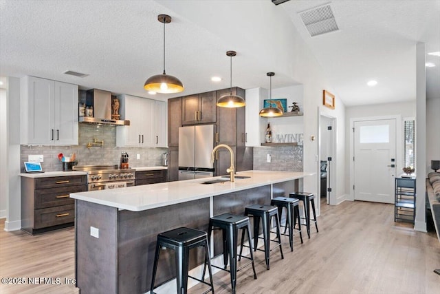 kitchen featuring sink, a breakfast bar area, hanging light fixtures, appliances with stainless steel finishes, and wall chimney range hood