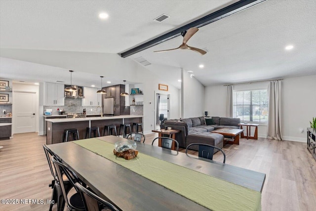 dining space featuring ceiling fan, lofted ceiling with beams, light hardwood / wood-style flooring, and a textured ceiling