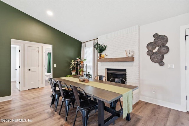 dining area with vaulted ceiling, a fireplace, and light wood-type flooring