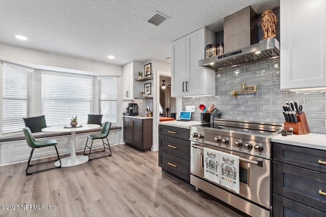 kitchen featuring white cabinets, backsplash, high end stainless steel range, light hardwood / wood-style floors, and wall chimney exhaust hood