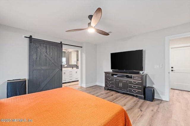 bedroom with ensuite bathroom, a barn door, hardwood / wood-style floors, and ceiling fan