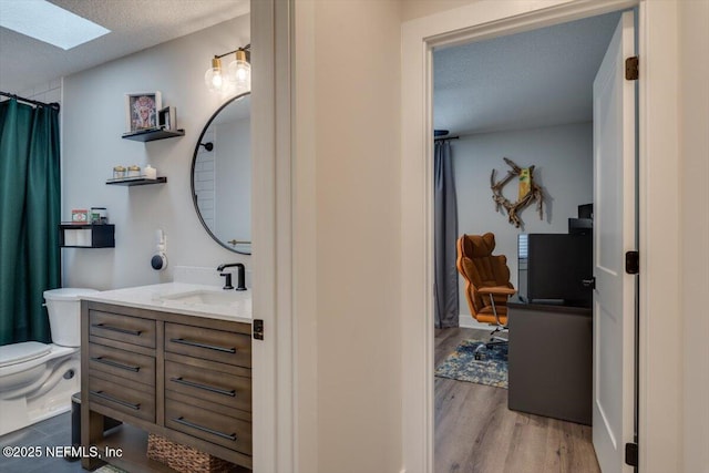 bathroom with a skylight, hardwood / wood-style flooring, vanity, toilet, and a textured ceiling