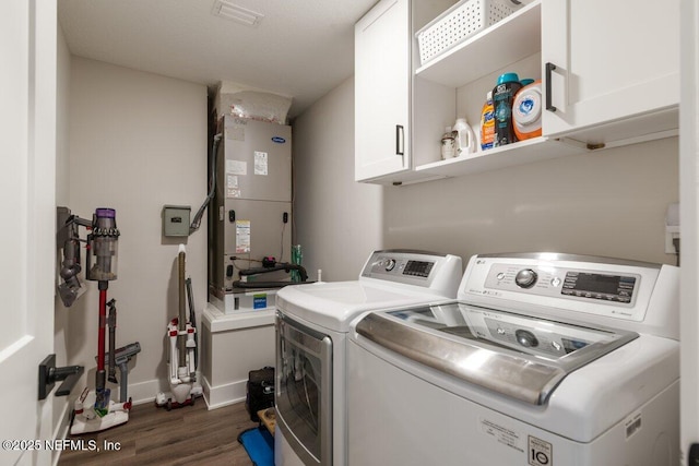 clothes washing area featuring heating unit, dark wood-type flooring, cabinets, and washing machine and clothes dryer