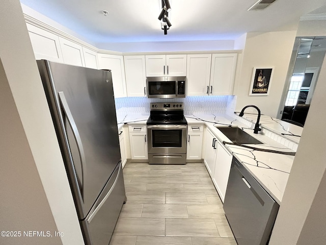 kitchen with sink, white cabinets, kitchen peninsula, stainless steel appliances, and light stone countertops