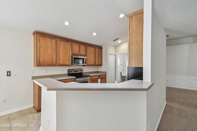 kitchen with light tile patterned floors, stainless steel appliances, kitchen peninsula, and a textured ceiling