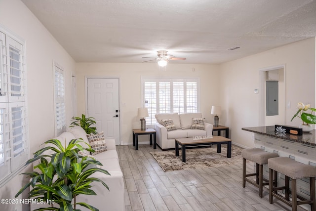 living room featuring ceiling fan, electric panel, a textured ceiling, and light hardwood / wood-style flooring