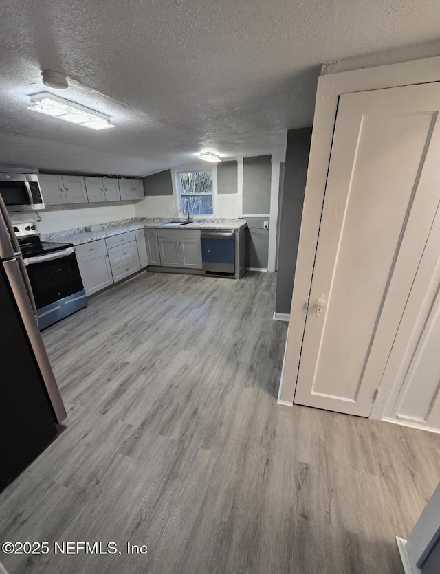 kitchen featuring sink, light wood-type flooring, light stone counters, stainless steel appliances, and a textured ceiling