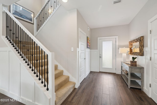 entrance foyer with dark wood-type flooring, visible vents, a decorative wall, and stairs