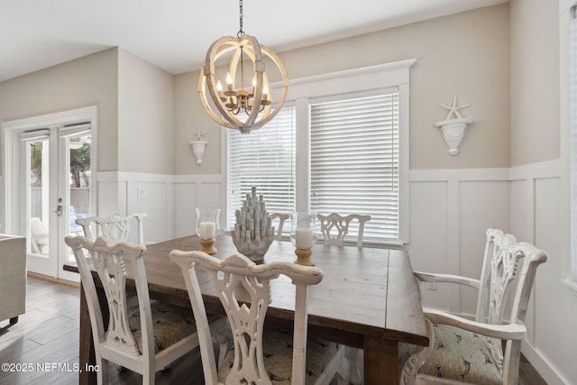 dining space featuring a wainscoted wall, a decorative wall, wood finished floors, and an inviting chandelier