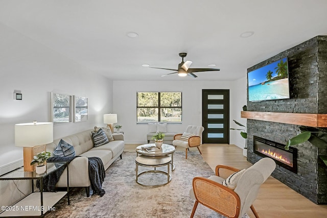 living room with light hardwood / wood-style floors, ceiling fan, and a stone fireplace
