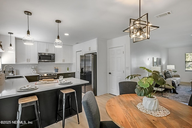 kitchen with appliances with stainless steel finishes, hanging light fixtures, a kitchen breakfast bar, white cabinets, and sink