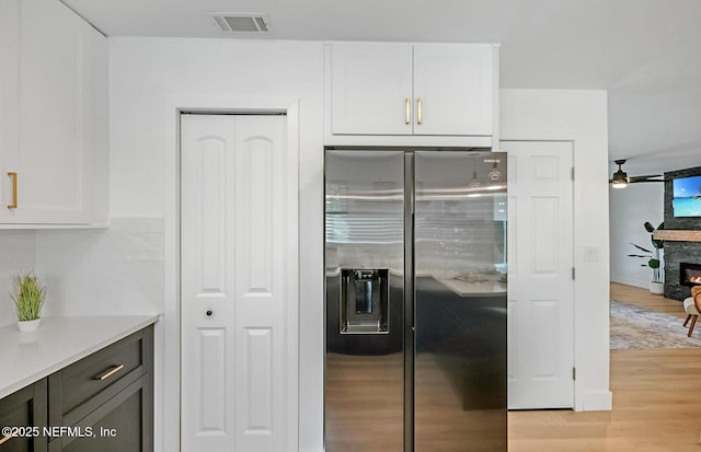 kitchen with stainless steel refrigerator with ice dispenser, decorative backsplash, light hardwood / wood-style floors, a fireplace, and white cabinetry