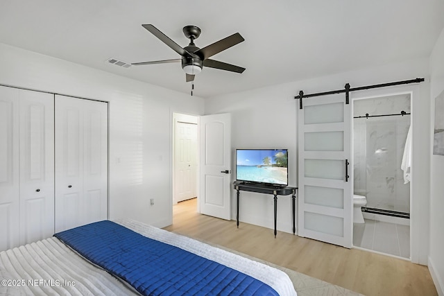 unfurnished bedroom with light hardwood / wood-style flooring, a closet, connected bathroom, ceiling fan, and a barn door