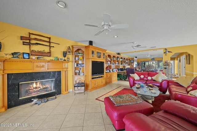 living room featuring ceiling fan, a fireplace, a textured ceiling, and light tile patterned floors