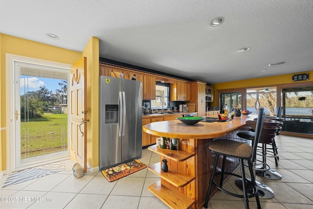 kitchen with sink, light tile patterned floors, a textured ceiling, and stainless steel fridge with ice dispenser