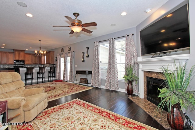 living room featuring a high end fireplace, dark hardwood / wood-style flooring, ceiling fan with notable chandelier, and a textured ceiling