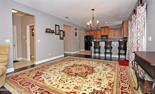 interior space with a breakfast bar, black appliances, a chandelier, hanging light fixtures, and backsplash