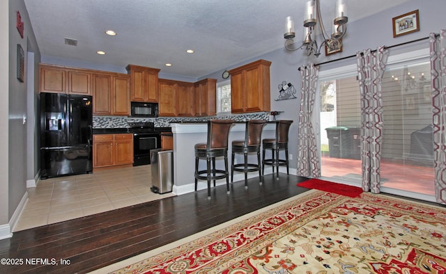 kitchen featuring a kitchen bar, a chandelier, light hardwood / wood-style floors, decorative backsplash, and black appliances