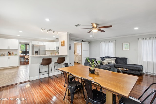 dining area with sink, crown molding, ceiling fan, a barn door, and light wood-type flooring