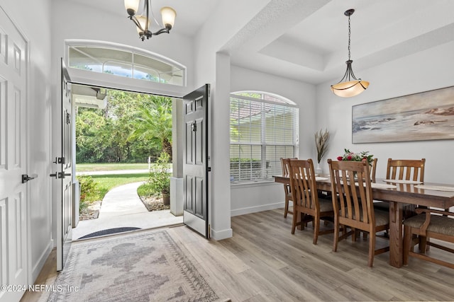 dining room with a raised ceiling, an inviting chandelier, and light wood-type flooring